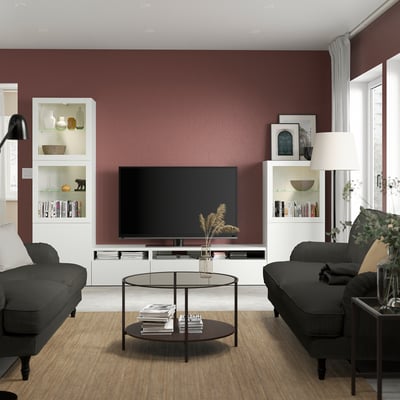 Modern living room with maroon wall, BESTÅ tv unit, grey sofas, and glass table.