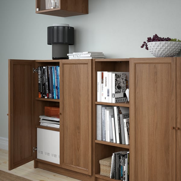Wooden bookshelf with glass doors holding books, a bowl of fruit, and a lamp.