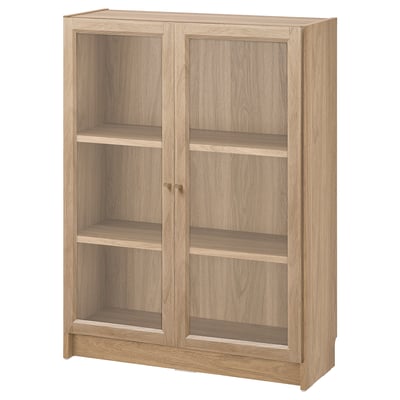 A BILLY wooden bookshelf with two glass doors. The light brown unit adjustable shelves, and a classic rectangular design.