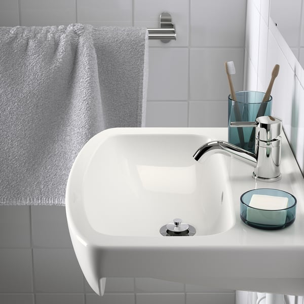 A sleek white washbasin with integrated drain stopper, featuring modern chrome tap, toothbrush holder with two toothbrushes, and a glass soap dish.