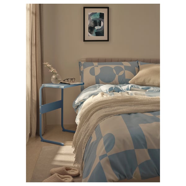 Blue metal side table next to bed, holding vase, glasses, and book.
