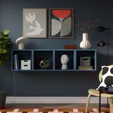 Aversely blue wall-mounted EKET shelves hold modern decor, chairs, and art near a dark blue wall.