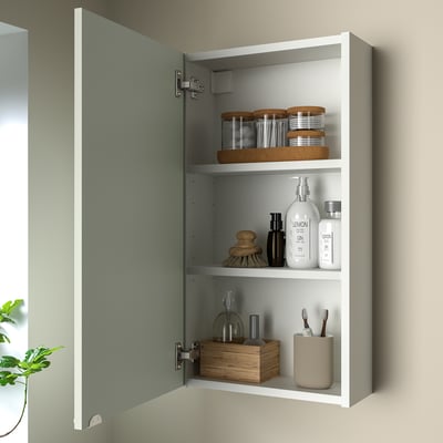 Open ENHET wall cabinet with green front, storing toiletries: jars, toothbrushes, bottles.