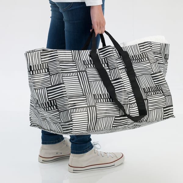Person holding large black and white striped bag. Bag appears durable and suitable for shopping or laundry.