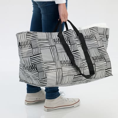 Person holding large black and white striped bag. Bag appears durable and suitable for shopping or laundry.