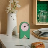Green FLODKRÄFTA clock on kitchen counter with vase and flowers.