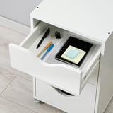 Open white drawer with office supplies: pens, notepad, sticky notes.