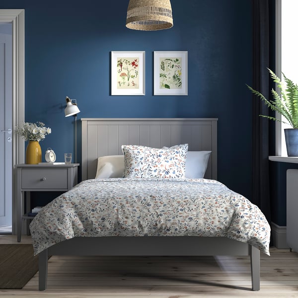 Cosy bedroom with GULLABERG bed, white & floral bedding, dark blue walls, bedside table with lamp, clock & vase.