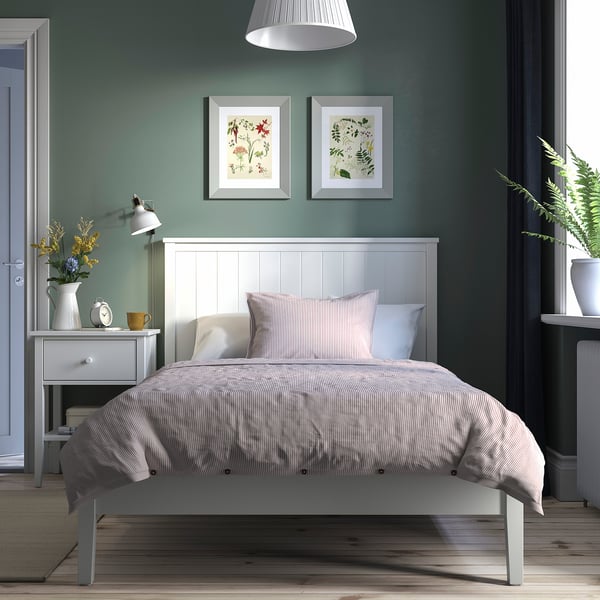 Gullberg bedroom: white bed, striped comforter, sage walls, floral art, bedside table with decor, wall lamp, potted plant.