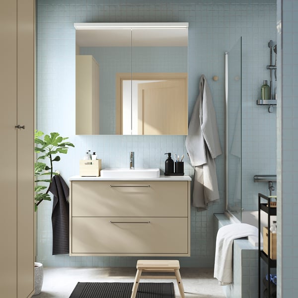 Modern bathroom with beige HAVBÄCK vanity, two drawers, ceramic sink, blue tiles, large mirror, small plant.