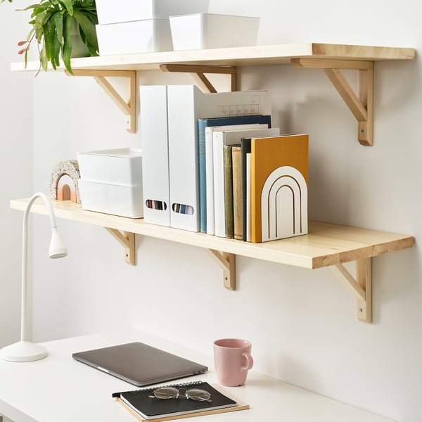 Home office setup with wooden shelves, books, boxes, laptop, lamp, mug and glasses.