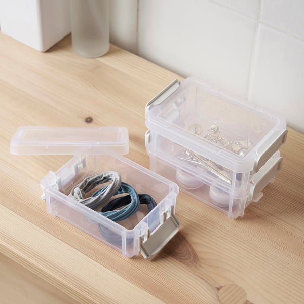 Two clear plastic HÖVAGN boxes on wood. One holds hair ties, the other small jewellery. Both have snap-on lids, showcasing organised storage.