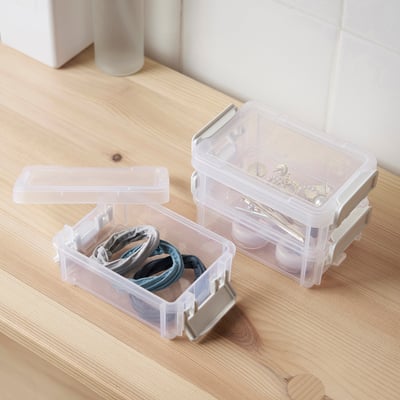 Two clear plastic HÖVAGN boxes on wood. One holds hair ties, the other small jewellery. Both have snap-on lids, showcasing organised storage.