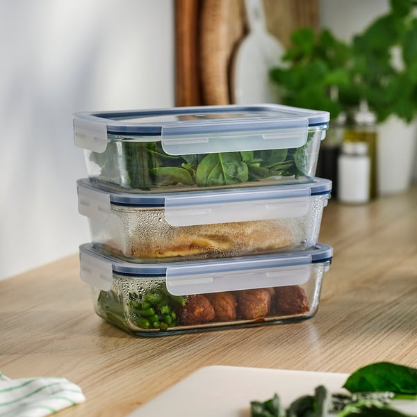 Three IKEA glass food containers with blue lids, holding food, ideal for meal prep and fridge storage.