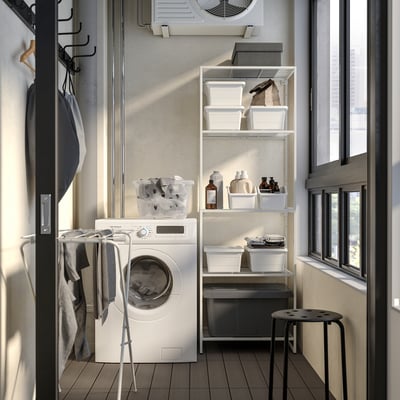 Small organised laundry room with white JOSTEIN shelves, holding plastic bins and cleaning supplies, next to a white washing machine and drying rack.