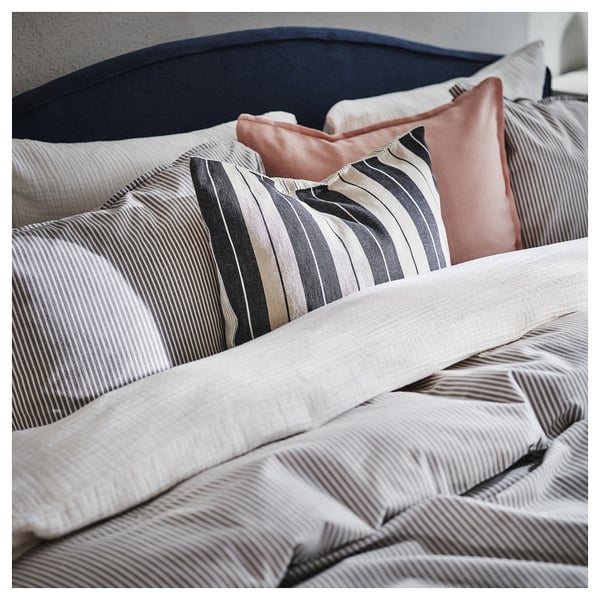 Cosy, striped cushions on a bed. Light beige and dark grey stripes, soft texture, rectangular shape.
