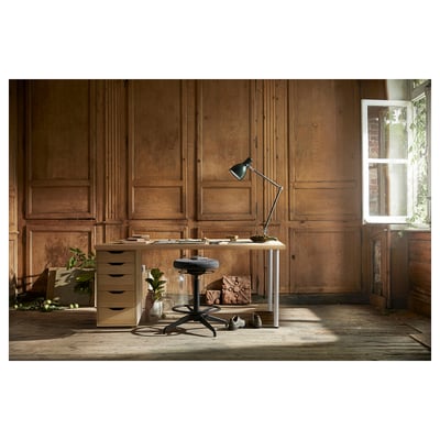 Desk setup with wooden panels, light-colored desk, black chair, and lamp.