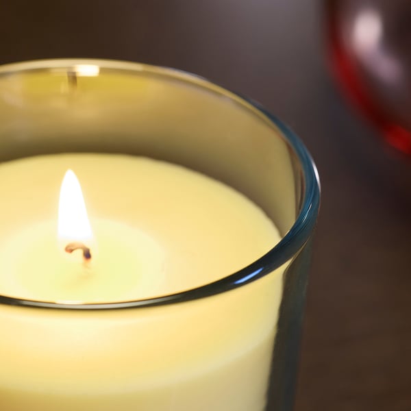 Lit scented candle in glass, yellow glow, steady flame.