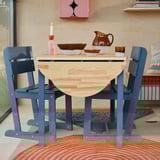 Dark blue rustic chair with pine seat, sled legs. Next to matching table, creating cosy dining area.