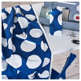 Blue fabric with white dots is being sewn on a machine. Scissors and a pin cushion are nearby on the table.