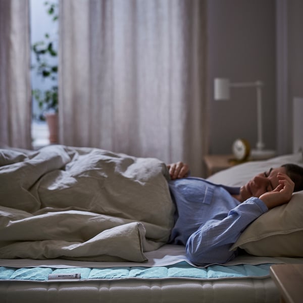A person on a bed with a REXBEGONIA cooling mattress protector, light-colored bedding, and a blue pillow.