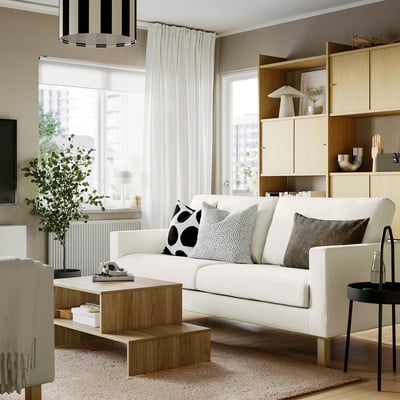 Modern living room with white sofa, pillows, coffee table, bookshelf, window curtains, side table, and rug.