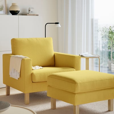 Bright yellow SALTSJÖBADEN armchair and ottoman, modern design, cosy and stylish, with wooden legs, positioned near a window.