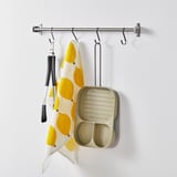 A kitchen hanging rod holds a lemon-patterned towel, kitchen tongs, and a three-sectioned non-stick frying pan.