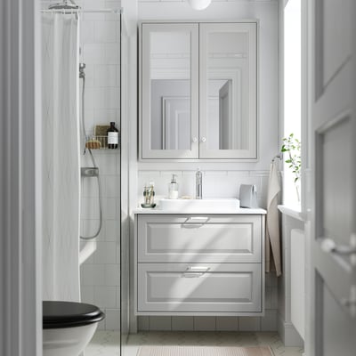 Modern white bathroom with light grey TÄNNFORSEN vanity, large mirror, sink, toilet, and shower.
