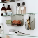 Glass bathroom shelves holding bottles, scrunchies, and hair tools.