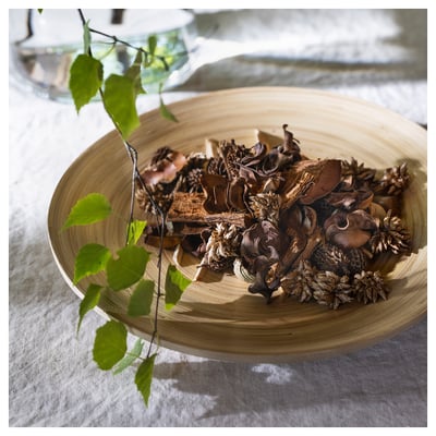 Wooden bowl of dried leaves and flowers, bright green branch, white cloth.