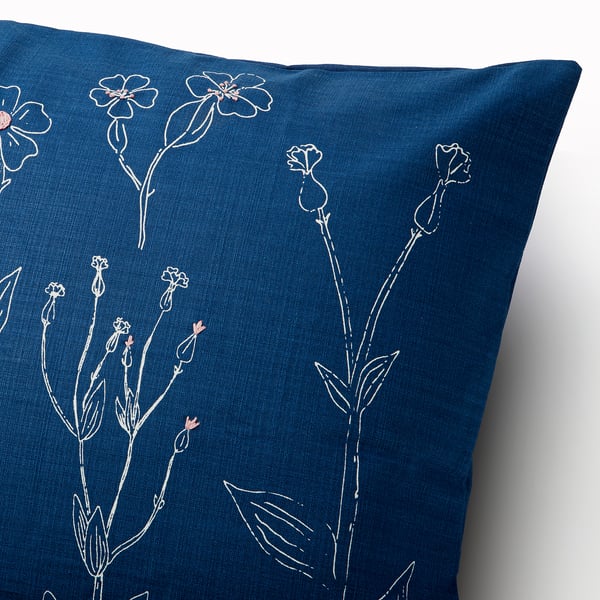 A square blue pillow with intricate, hand-embroidered white floral designs.