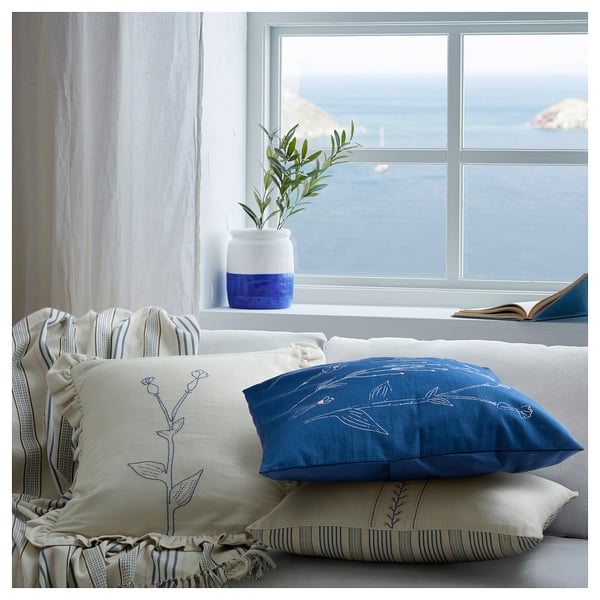 Bright living room setup by window with blue and white pillows, a blue vase, and a sea view.