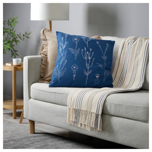 Grey sofa with blue pillow, beige blanket, lamp, side table.