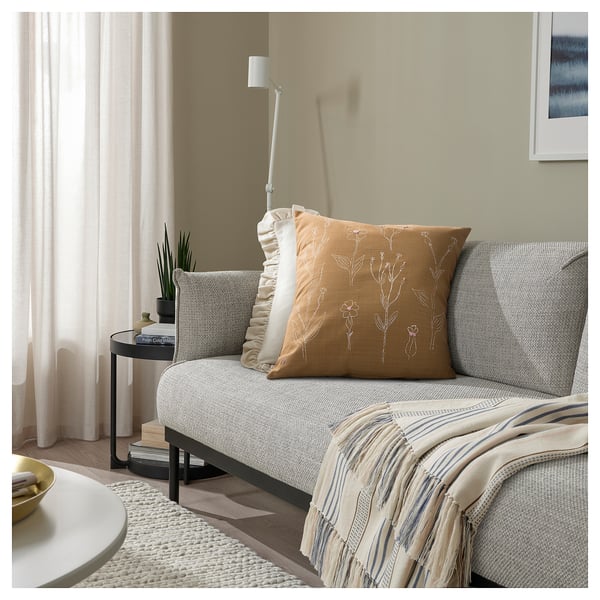 Cosy living room with light sofa, floral pillow, striped blanket, and plant.