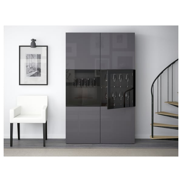 Modern storage cabinet with glass doors, holding wine glasses, next to white chair and staircase.