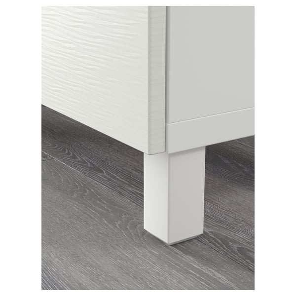 Close-up of modern, white BESTÅ furniture leg on wooden floor.