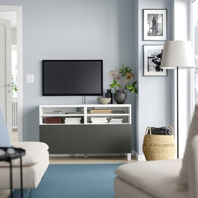 Modern living room with BESTÅ tv bench in white and black, featuring a flat-screen tv, decorative items, and a blue rug.