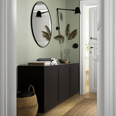 Modern hallway with BESTÅ unit, black cabinet against green wall, mirror, books, and decor.