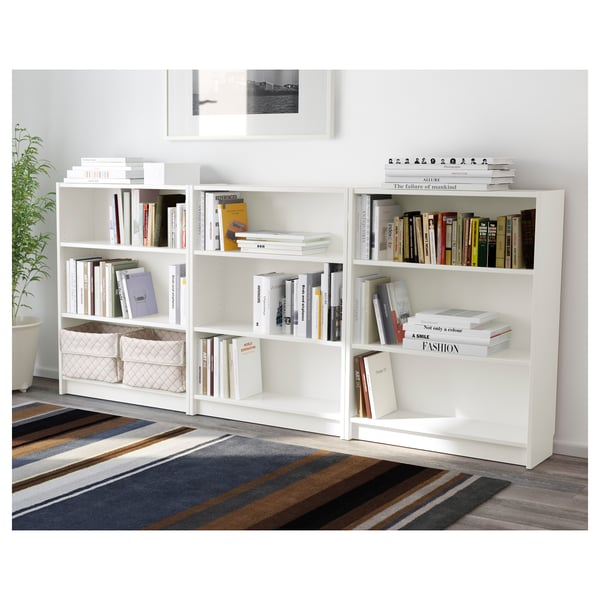 White BILLY bookcases with adjustable shelves full of books. A plant and striped rug beneath, a framed photo hangs above.