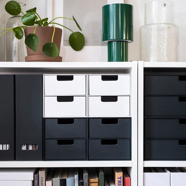 Modern bookcase BILLY with colourful drawers. White & black, holds books & decor. Plant & vases on top.