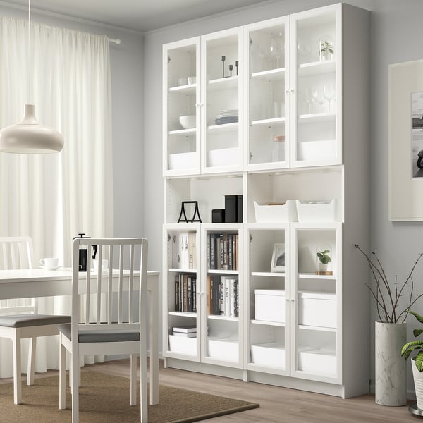 Modern living room with white BILLY bookcase, glass doors, various decorative items, and minimalist furniture. Bookcase occupies most of wall height.