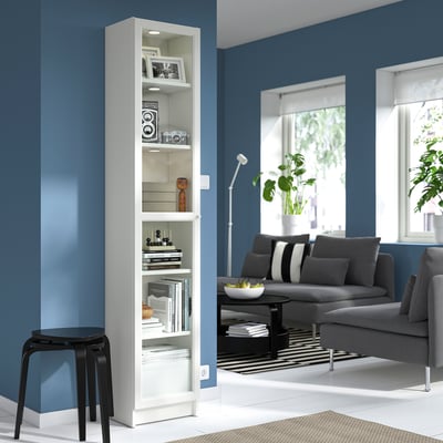 Modern living room with BILLY white bookcase, grey sofa, black stool, blue walls.
