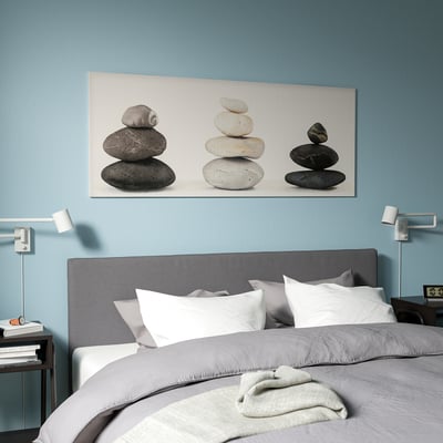 Blue walls, stone art, modern sconces above grey bed.