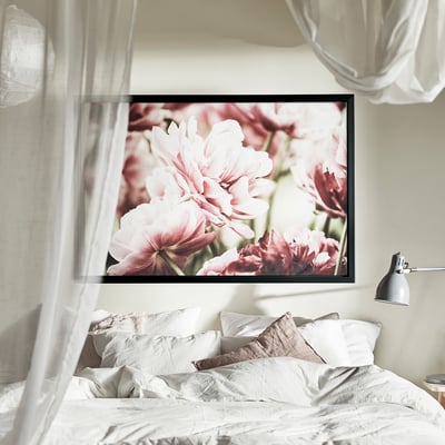 Cosy bedroom with large framed flower photo above messy white bed, wall-mounted grey lamp.
