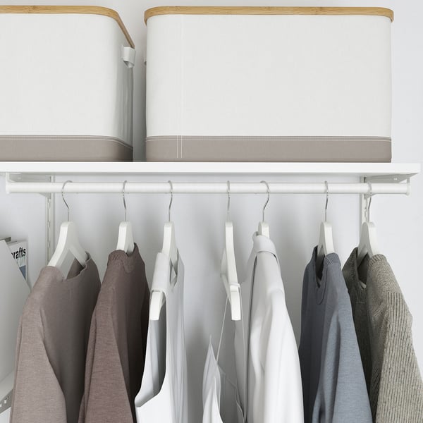 A closet with white hangers holding various clothes below shelves with white fabric storage boxes.