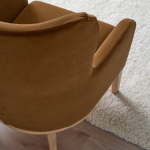 Brown velvet armchair with wooden legs on a shaggy rug. Upholstery appears soft, comfortable, and well-crafted.