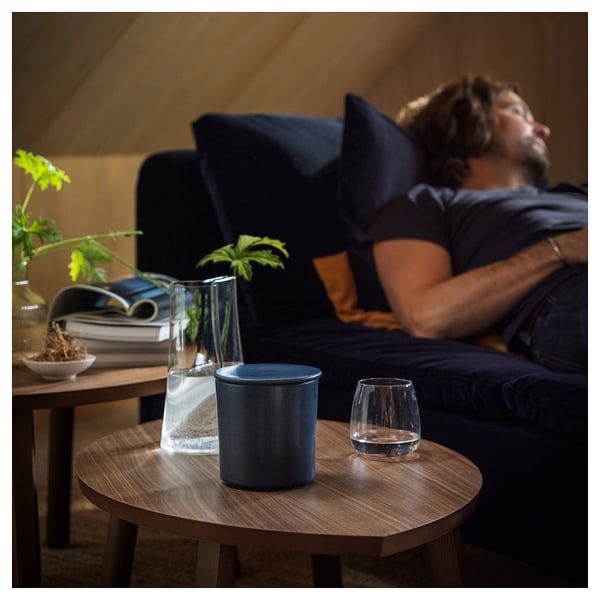 Cosy scene: person relaxes on dark couch, wood coffee table holds books, vases, candle, and glass.