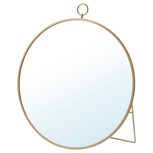 A round, brass-colored GRYTÅS mirror with a metal frame and stand. It can hang or stand, adding elegance to any space.