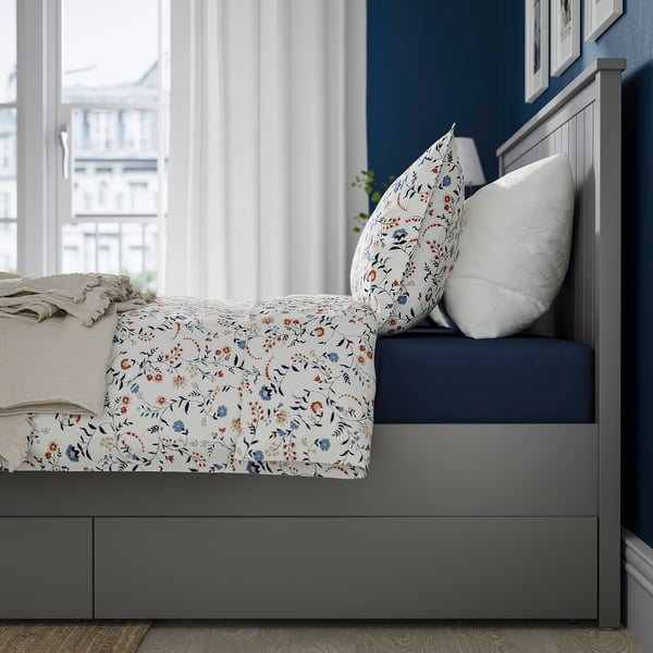 Bed with floral duvet, white pillows, dark frame, and large drawers on castors for storage.